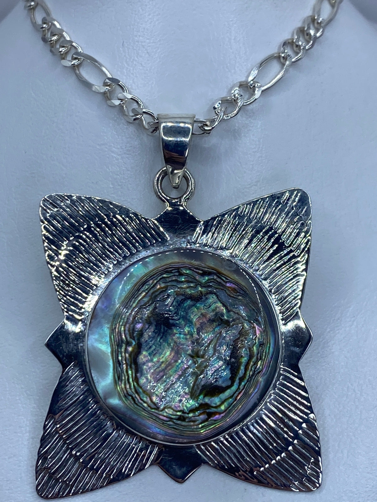 Detalle frontal del dije mostrando el reflejo azul-verde-púrpura de la concha de abulón engastada