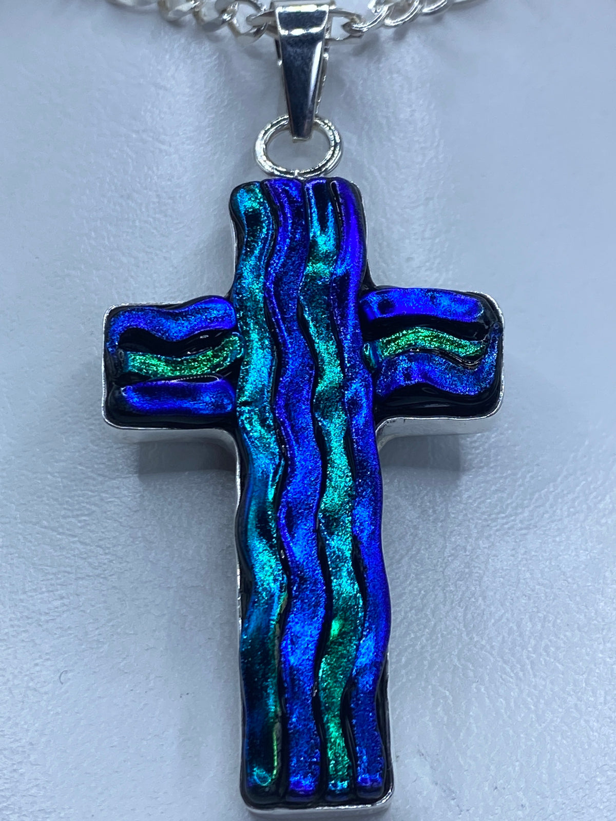 Detalle frontal de la cruz mostrando la incrustación decorativa con destellos azules y verdeazulados