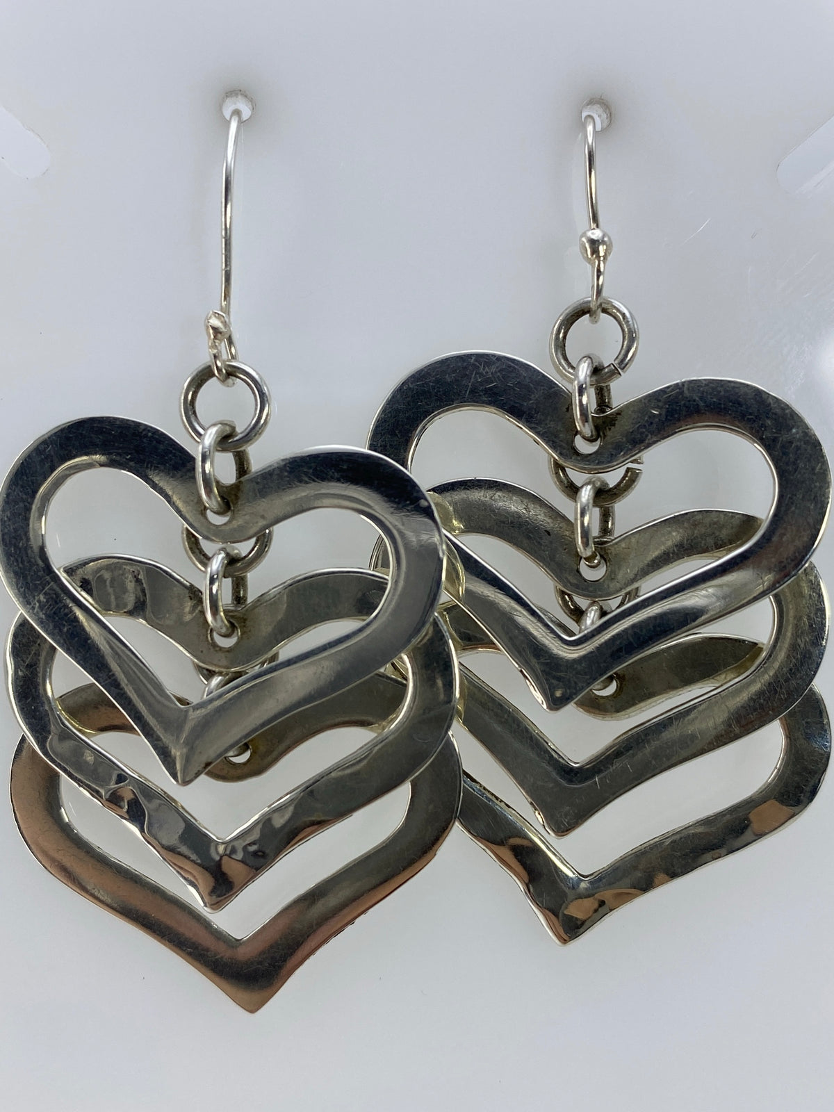 Vista frontal de los aretes de corazones de plata apilados reflejando luz