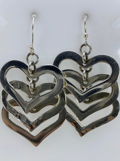 Vista frontal de los aretes de corazones de plata apilados reflejando luz