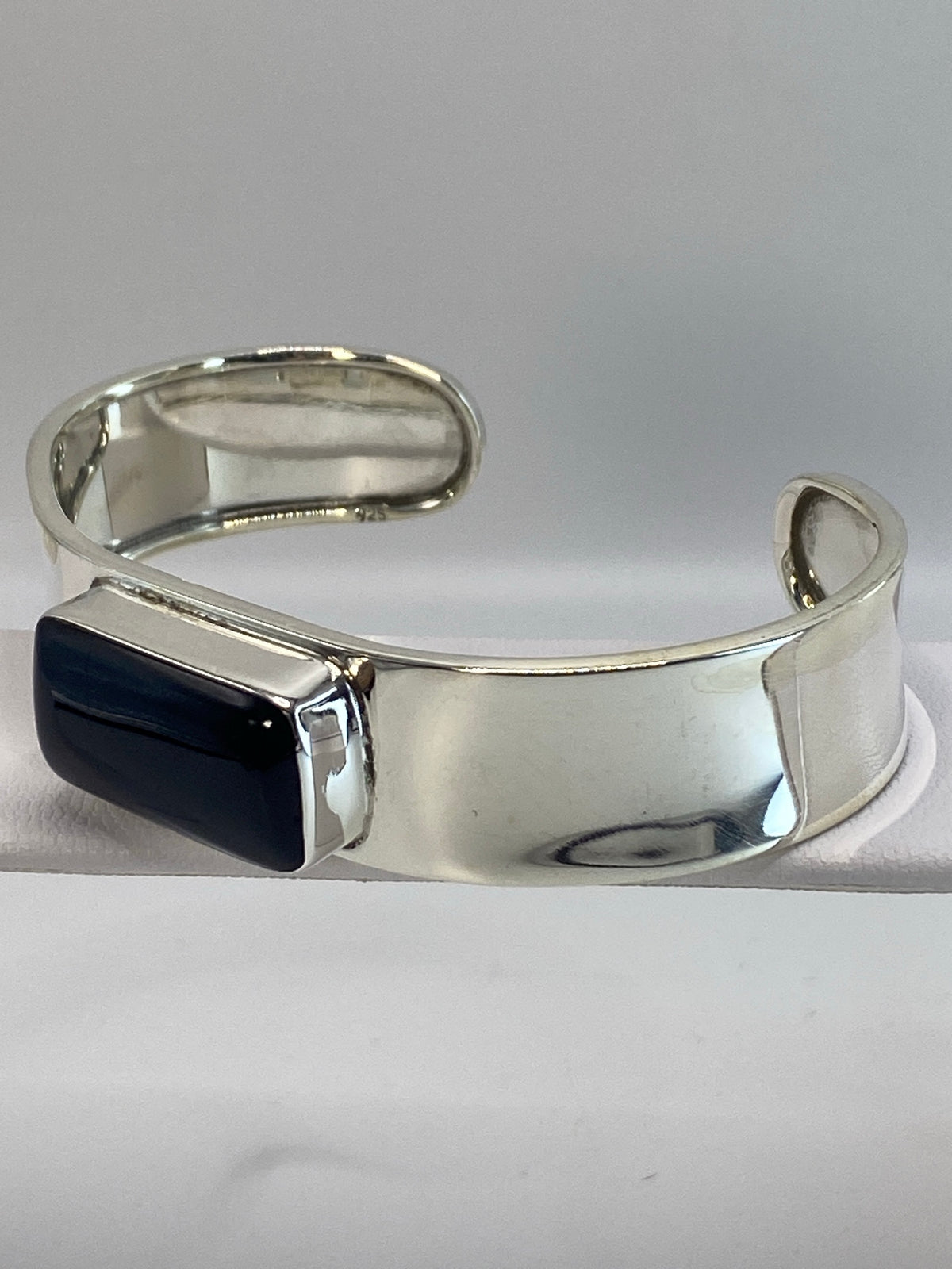 Brazalete de plata deslizándose sobre la muñeca, con la piedra ónix negra centrada en la banda ancha