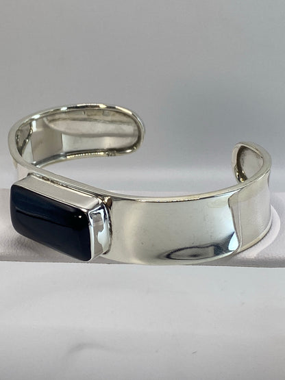 Brazalete de plata deslizándose sobre la muñeca, con la piedra ónix negra centrada en la banda ancha
