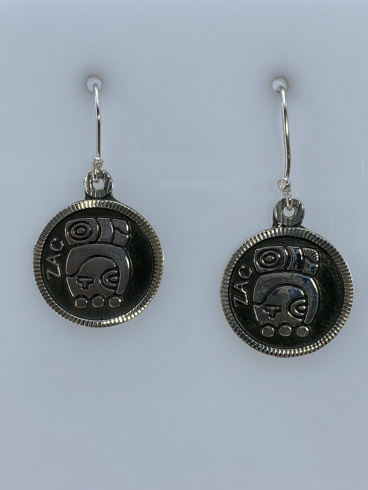 Par de aretes de plata repujado con motivo prehispánico de Taxco colgando del gancho