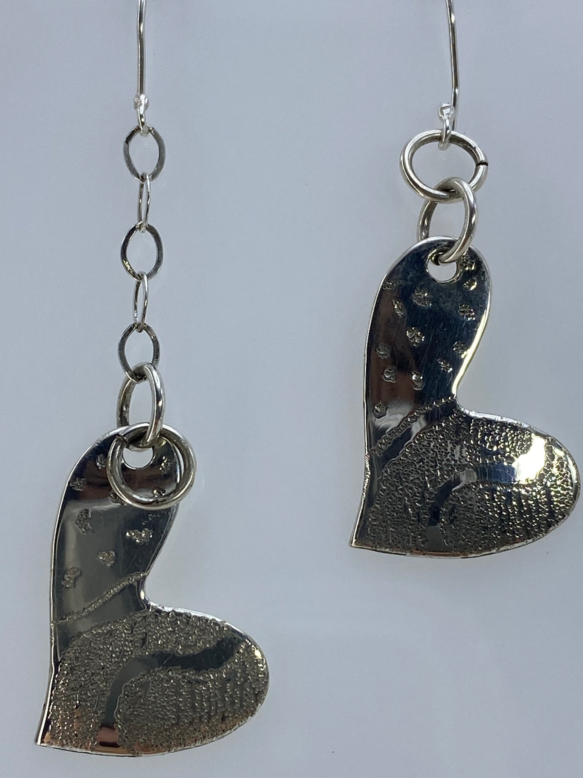 Aretes colgando sobre fondo blanco, vista frontal de los corazones de plata