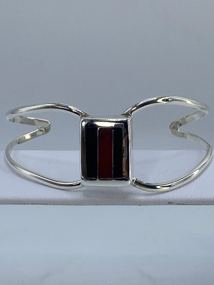 Brazalete de plata rígido con coral rojo e ónix negro en la muñeca de una mujer