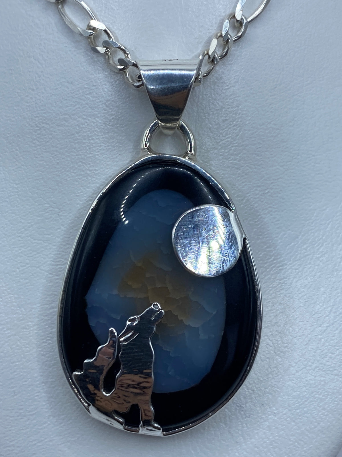 Vista frontal del dije lobo y luna mostrando el relieve y el engaste de onix