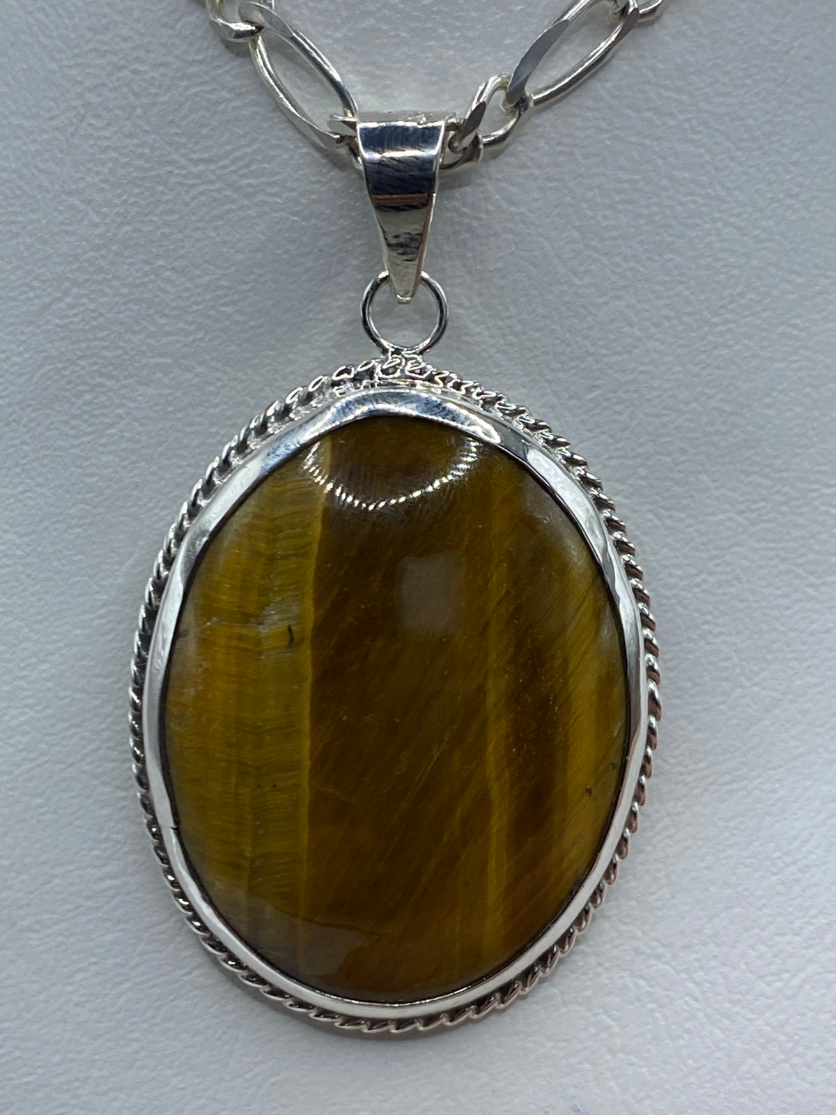 Dije de plata con Ojo de Tigre café en cordón plateado, sobre fondo blanco