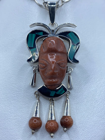 Dije prehispánico de plata repujada con rostro de Pakal, enmarcado en malaquita verde y ónix negro
