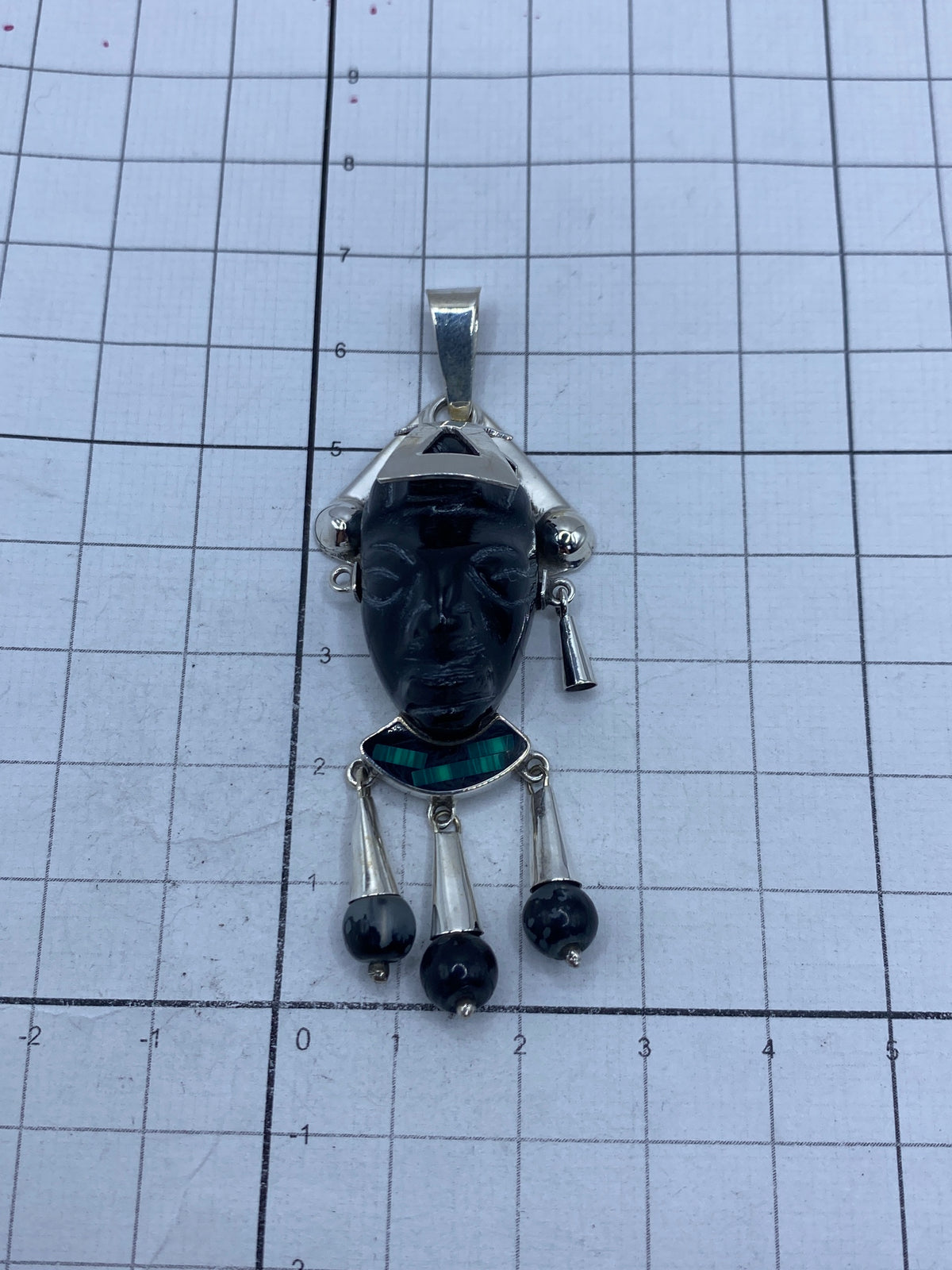 Dije de 6.7 cm sobre escala de medición, con tres perlas de ónix colgantes