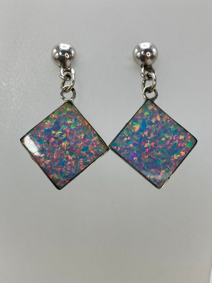 Aretes de plata con ópalo de fuego multicolor colgando sobre fondo blanco, mostrando los destellos de color