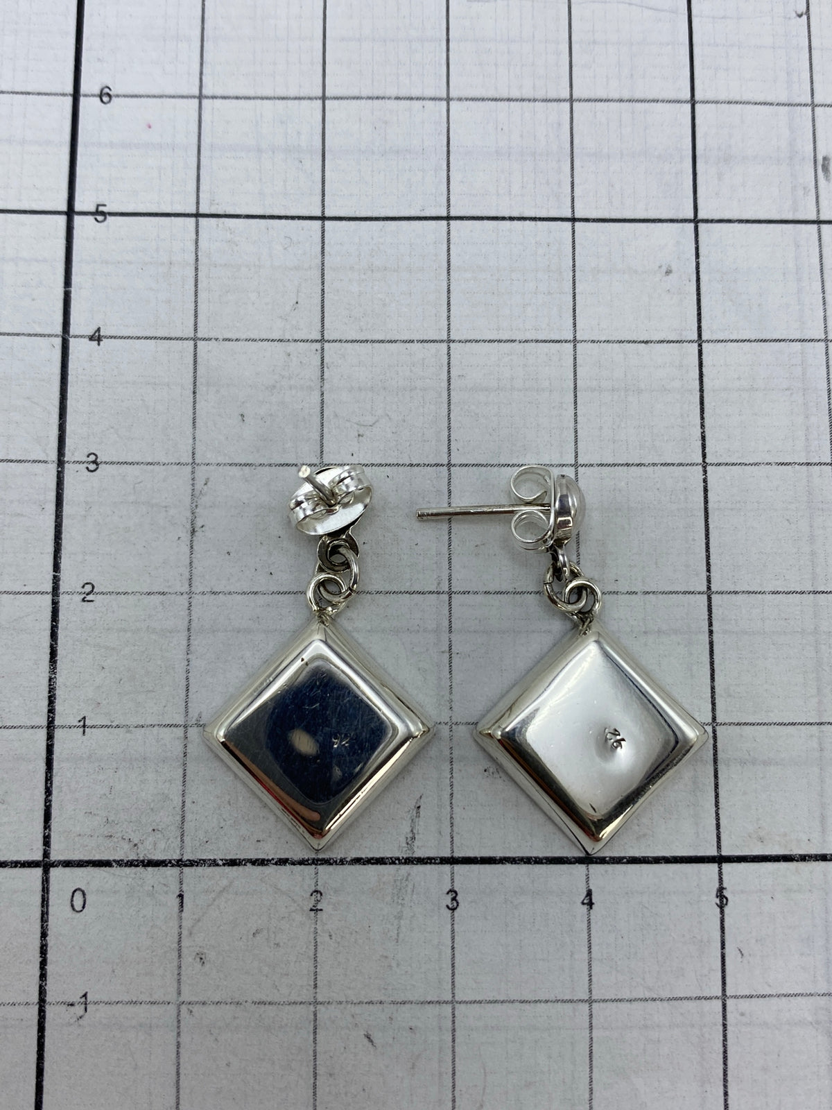 Comparativa de tamaño: los aretes miden 1.3 cm de largo junto a una regla de centímetros