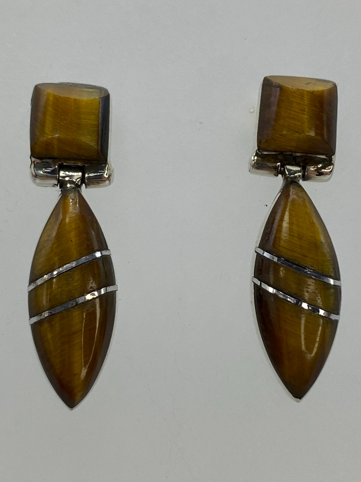 Aretes sobre paño azul mostrando la chatoyancia dorada del Ojo de Tigre