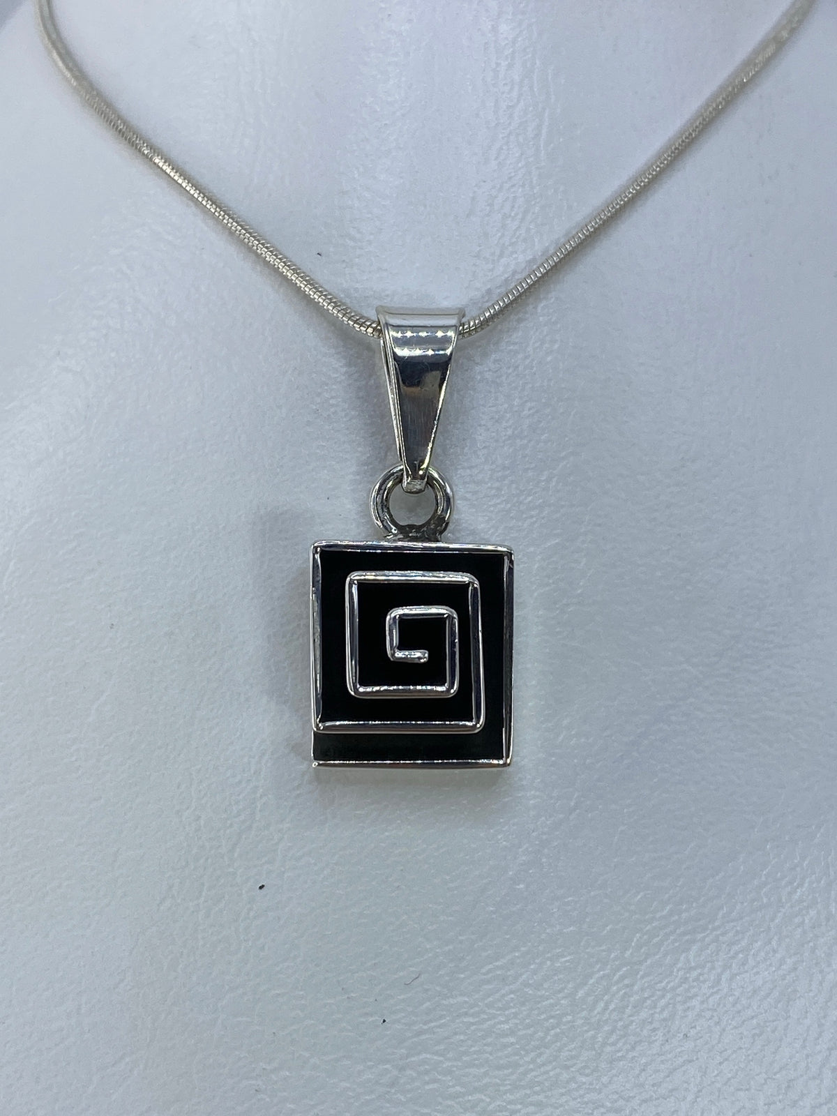 Dije de plata con espiral cuadrada concéntrica calada, colgando de cadena de eslabones