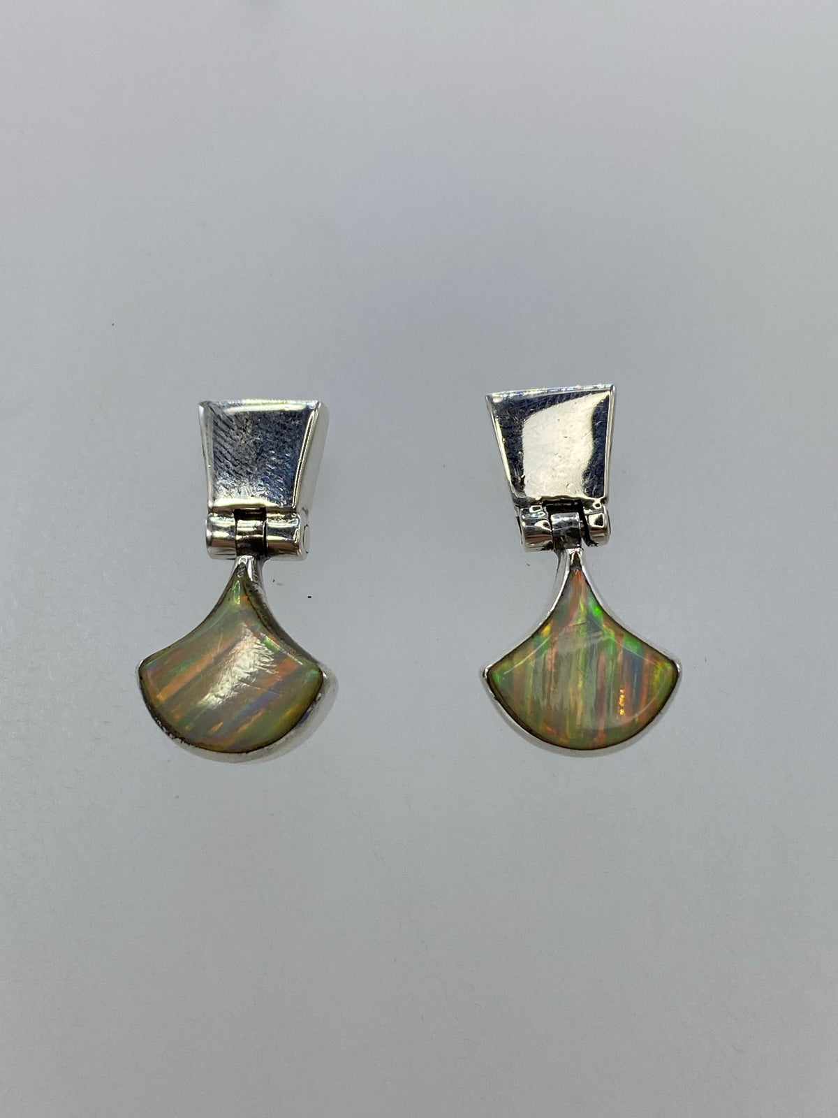 Detalle frontal de los aretes mostrando el engaste a mano del ópalo de fuego en plata