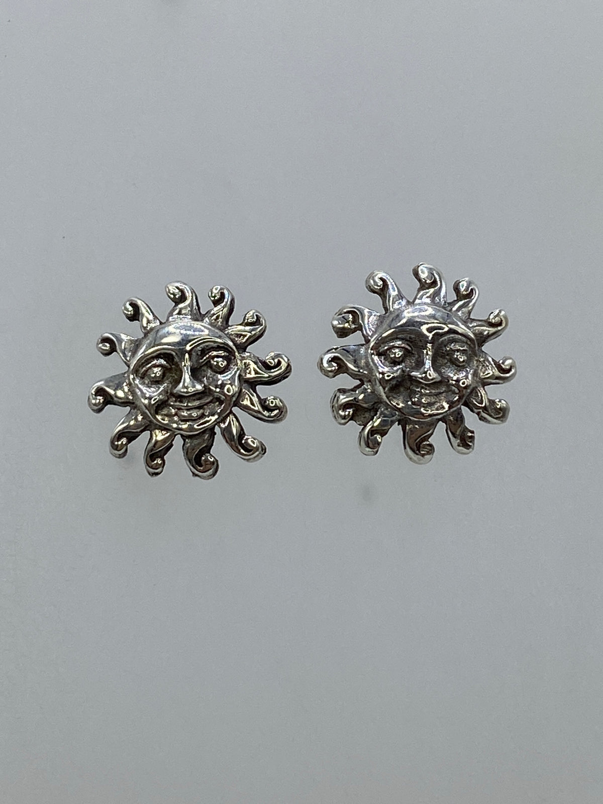Aretes de plata sol sonriente sobre fondo gris, lado izquierdo y derecho