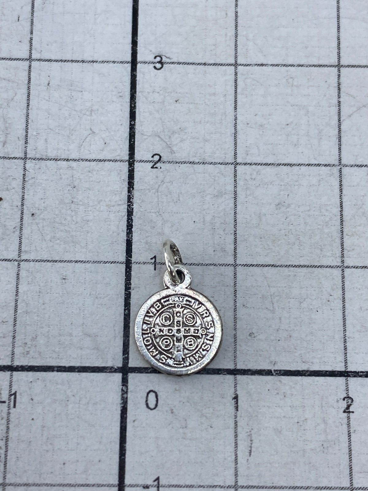Dije San Benito junto a regla de medida mostrando tamaño de 1.3 cm de largo