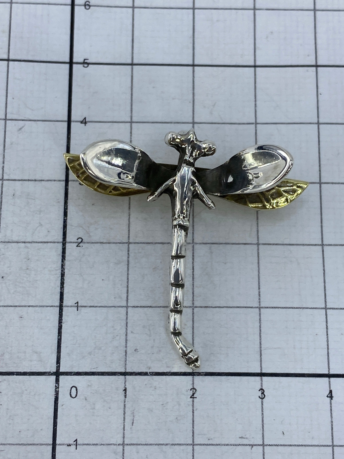 Dije libélula junto a escala en centímetros mostrando tamaño real de 3.7 × 3.8 cm