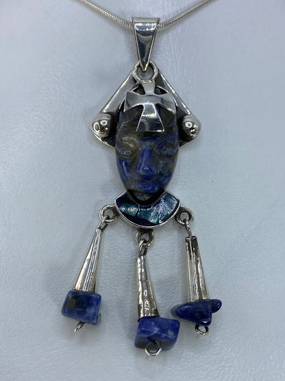 Dije de plata con cabeza azteca tallada y piedra azul engastada, colgando de cadena de plata