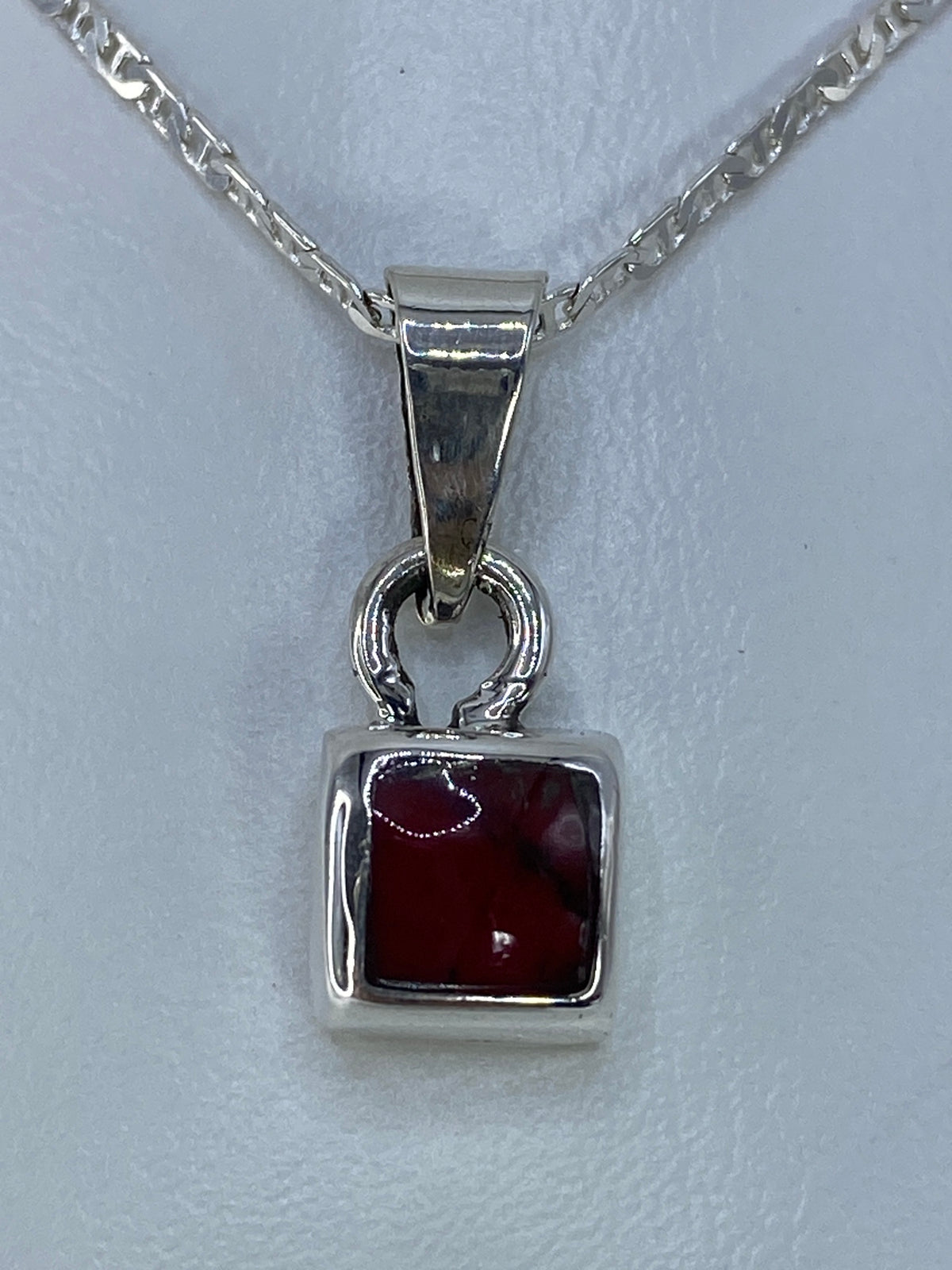 Dije de plata 925 con coral rojo engastado, visto de frente sobre cadena plateada