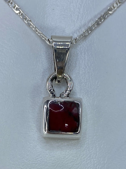 Dije de plata 925 con coral rojo engastado, visto de frente sobre cadena plateada