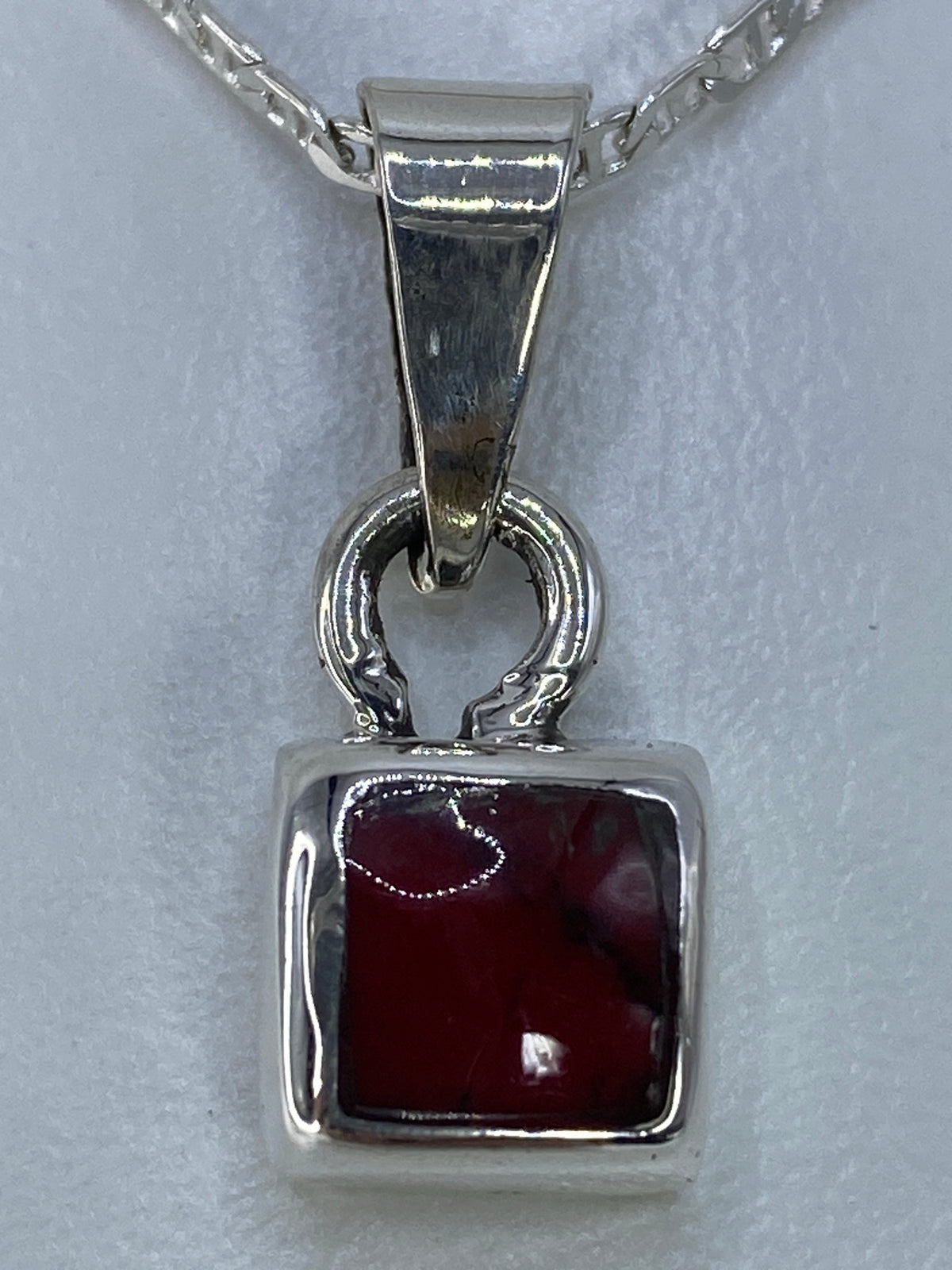 Dije de plata con coral sobre escala, midiendo 2.5 cm de largo