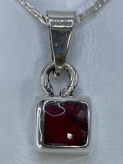 Dije de plata con coral sobre escala, midiendo 2.5 cm de largo