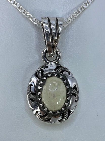 Dije de plata ovalado con piedra blanca engastada y diseño de águila, colgado de cadena plateada