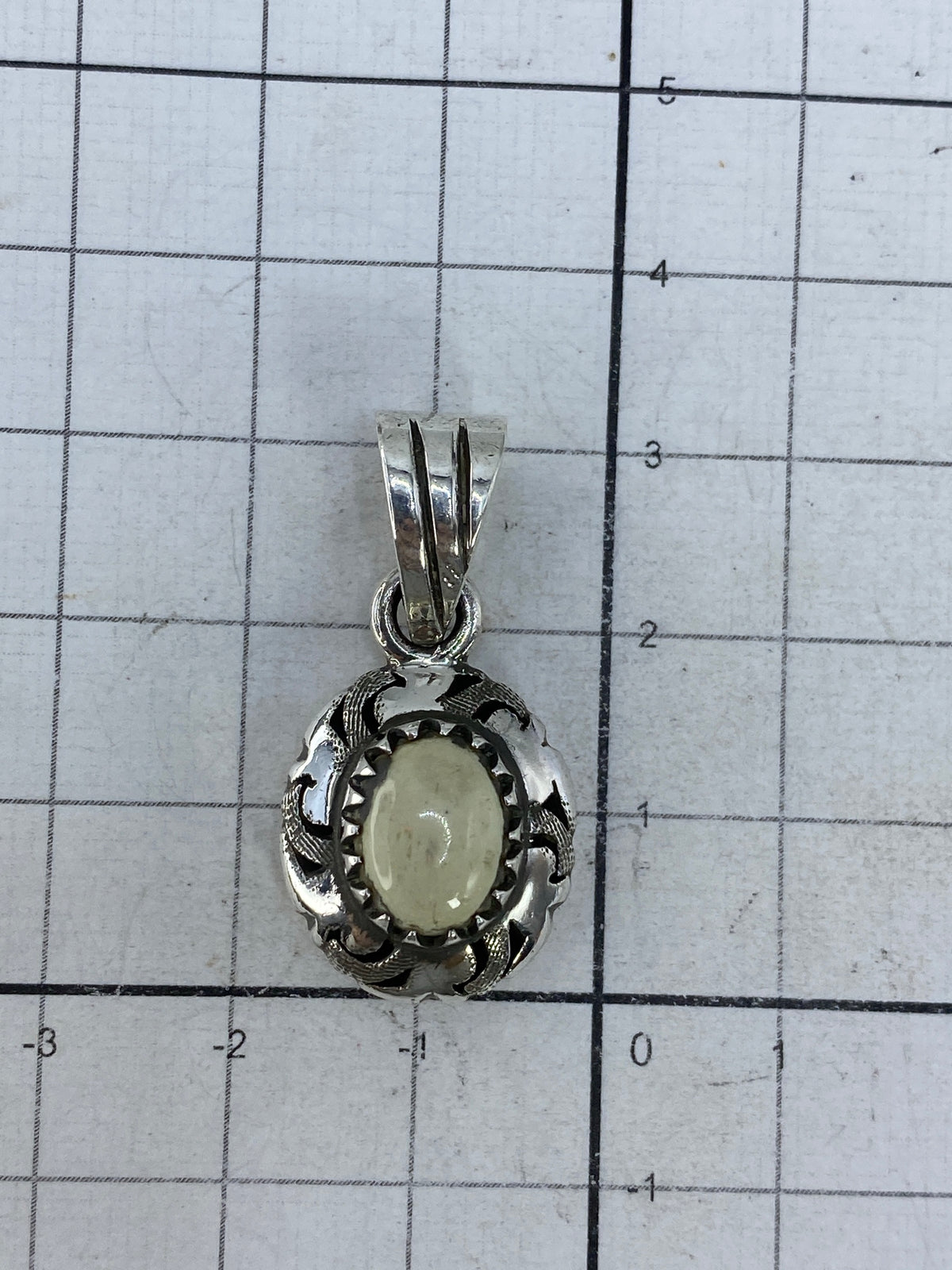 Dije de plata sobre fondo blanco con escala de centímetros, tamaño 3.1 cm
