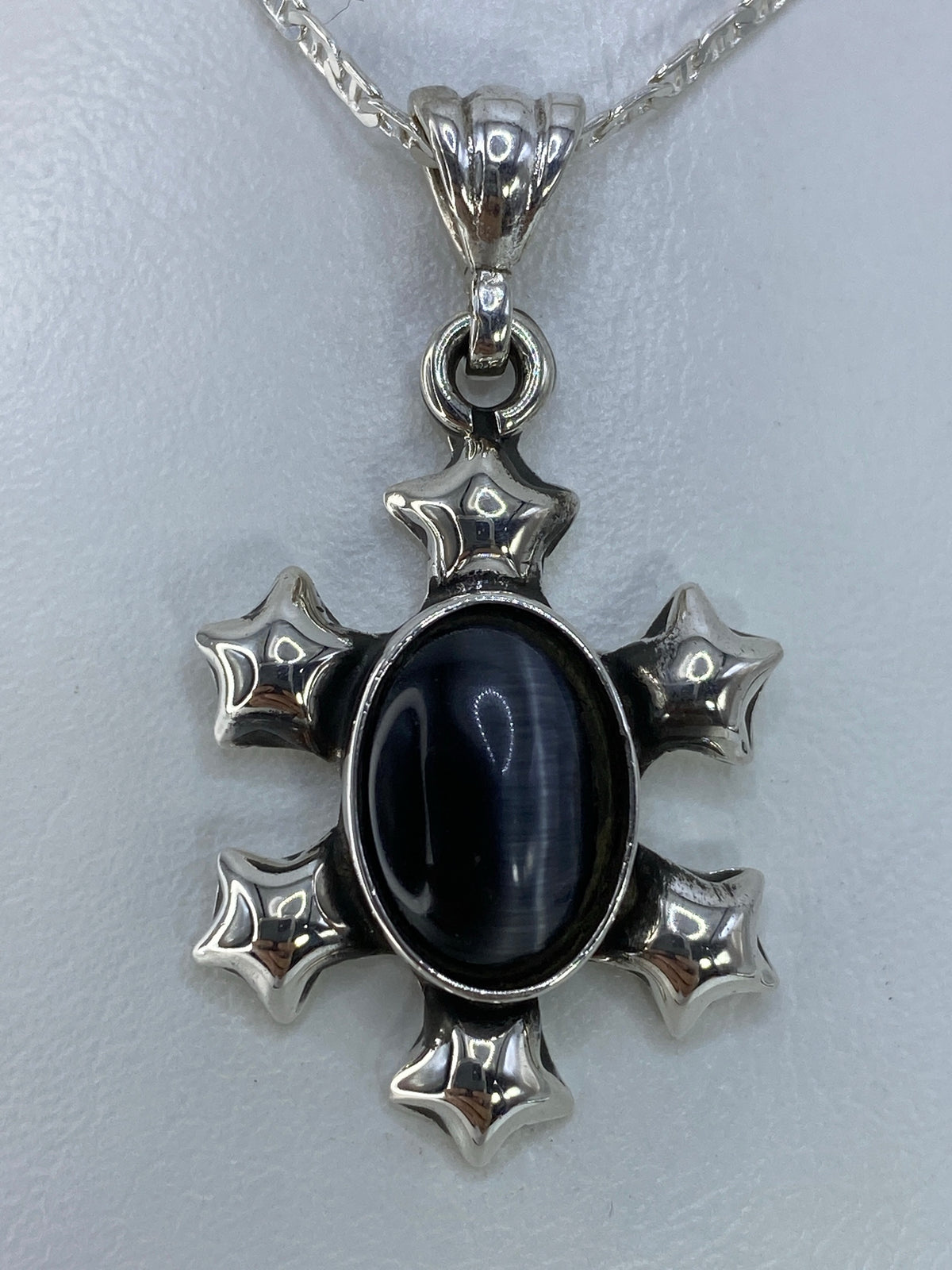 Dije cruz de plata con Ojo de Gato negro engastado en el centro, sobre cadena de eslabones