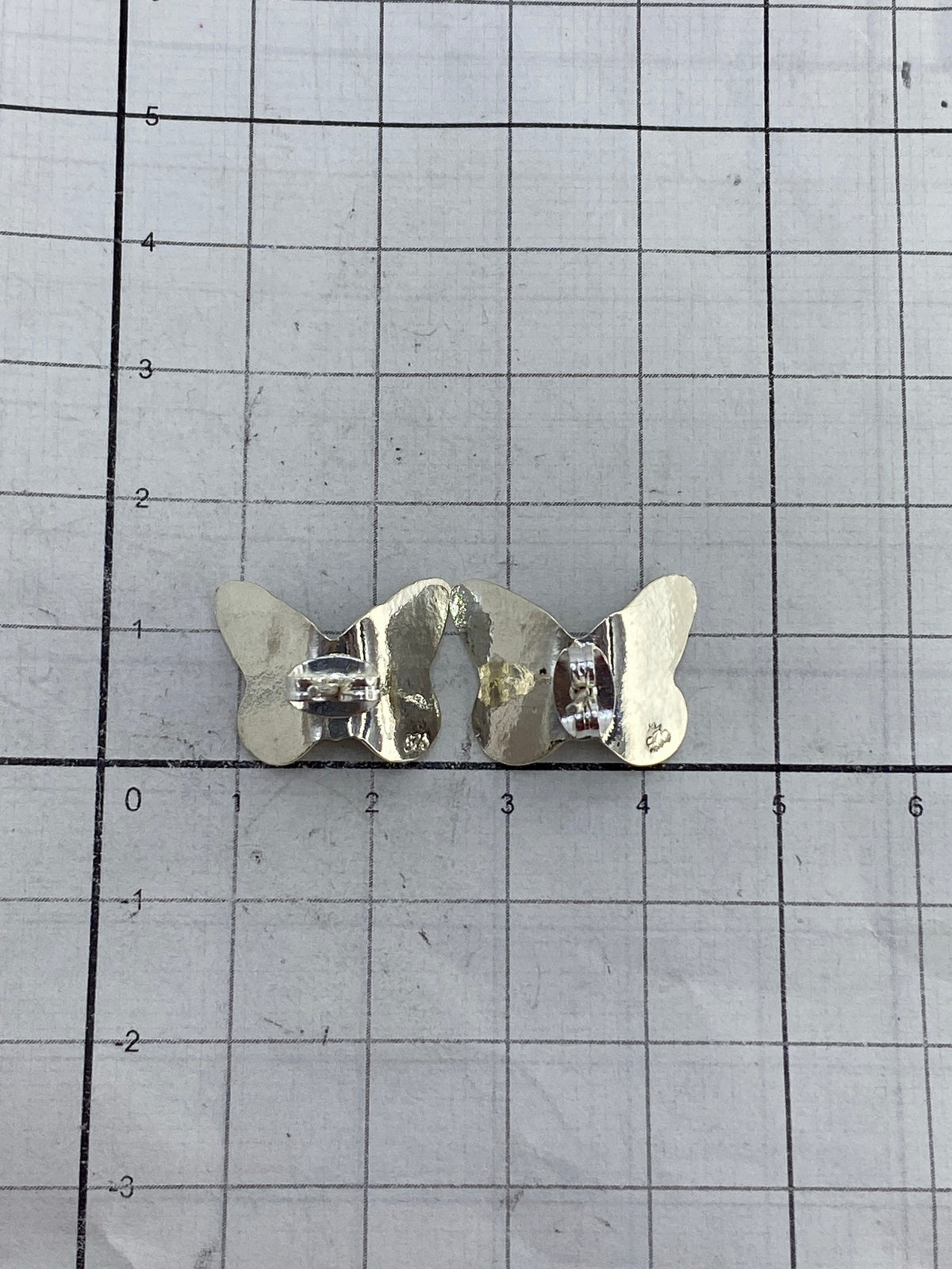 Aretes de mariposa sobre fondo gris mostrando el acabado pulido de la plata 925