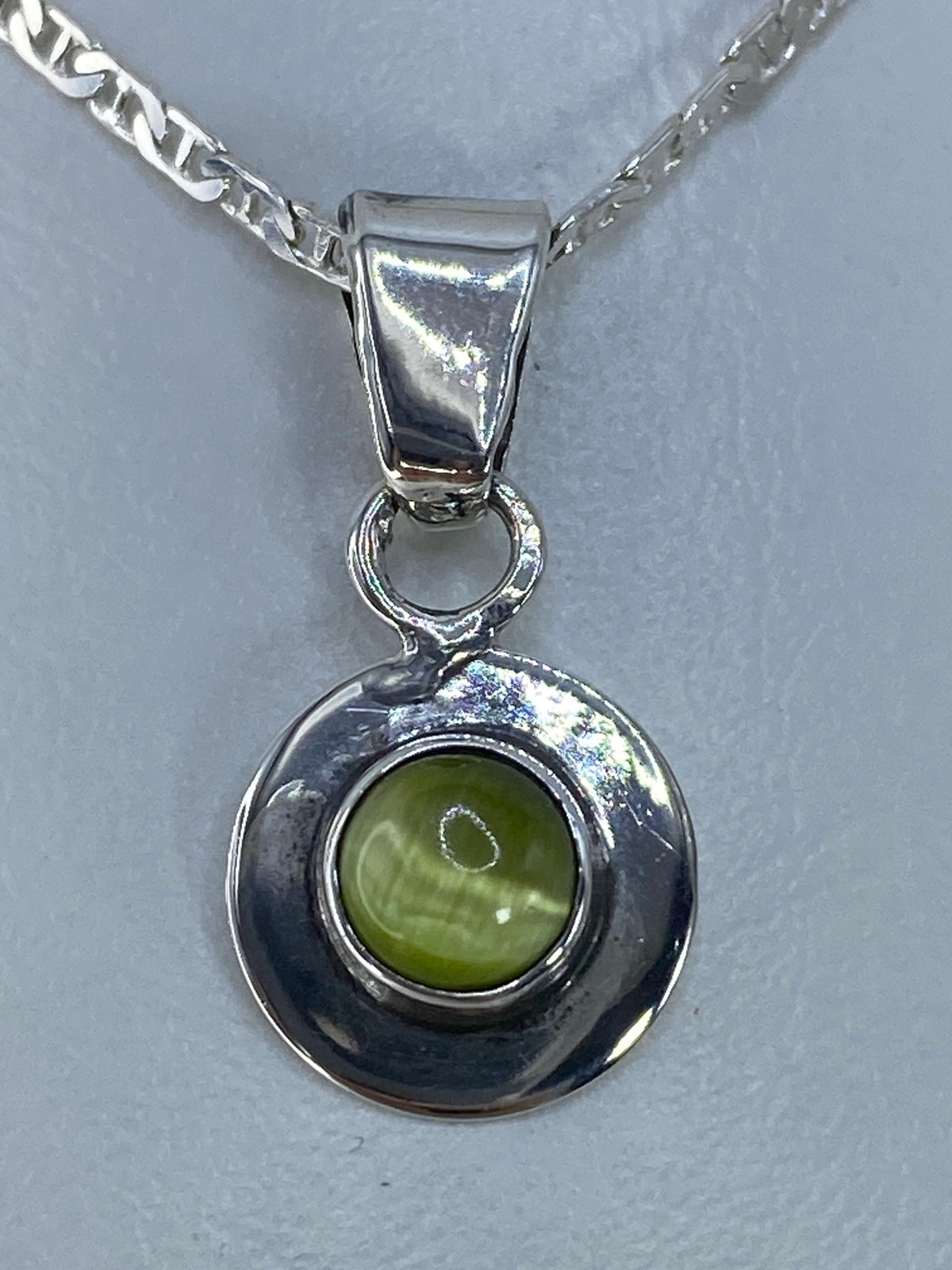 Dije de plata con Ojo de Gato verde olivo engastado, colgando de una cadena plateada