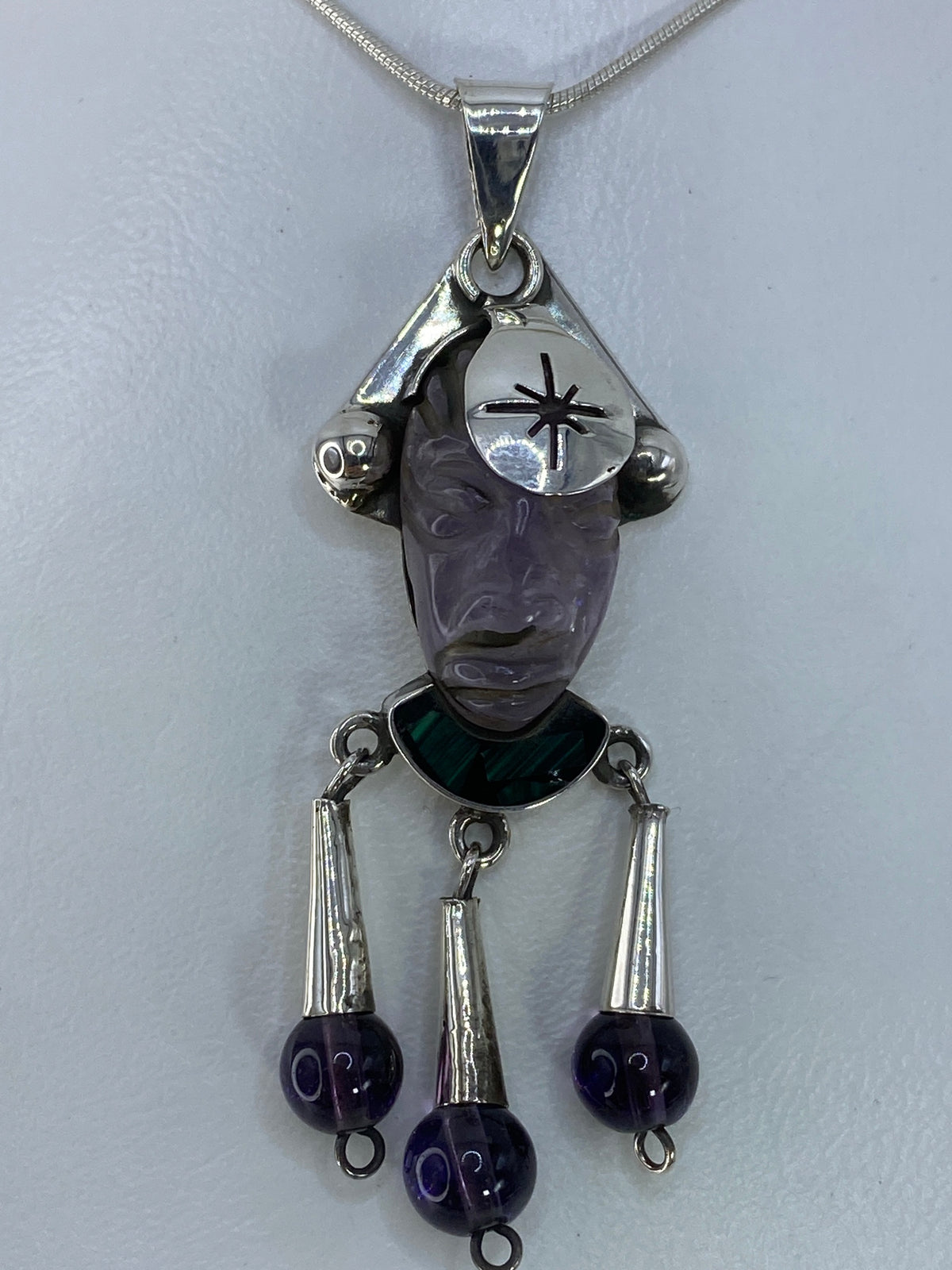 Dije de plata con rostro tallado y amatista morada en la frente, con tres esferas colgantes
