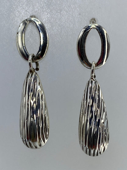 Par de aretes de plata cartoneado con forma de gota colgando en primer plano