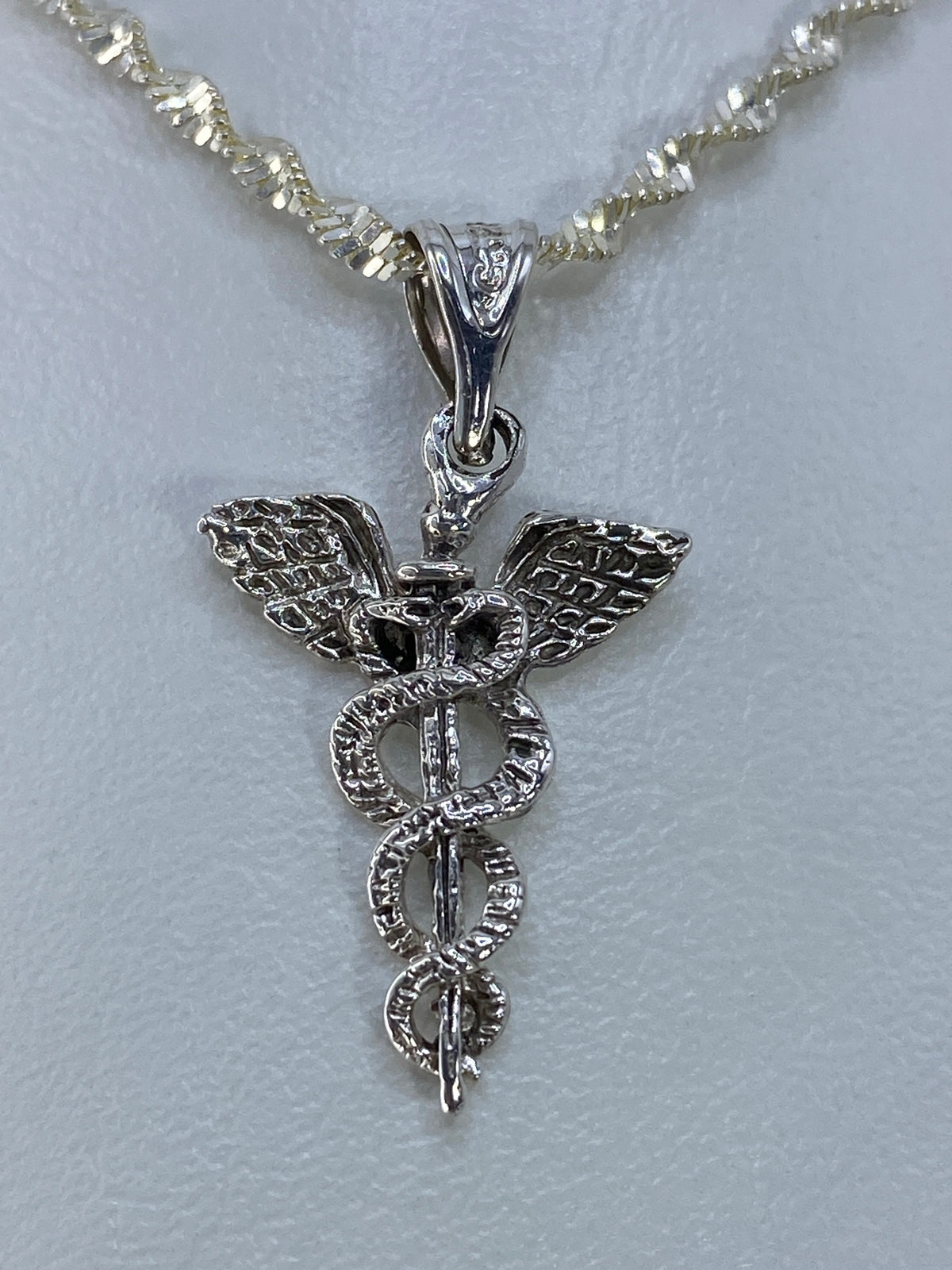 Dije caduceo sobre regla mostrando 2.8 cm de largo