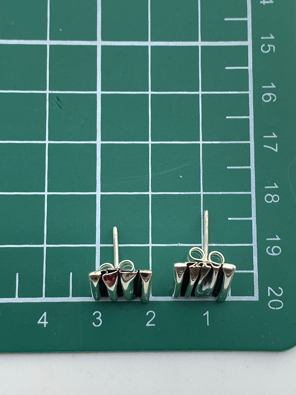 Aretes de plata maciza sin piedra sobre fondo neutro con medida de referencia