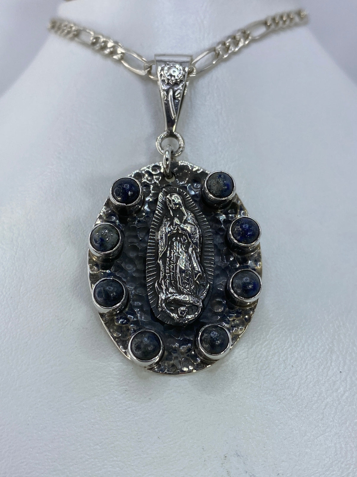 Lateral del dije religioso mostrando la profundidad del repujado y el detalle de las piedras