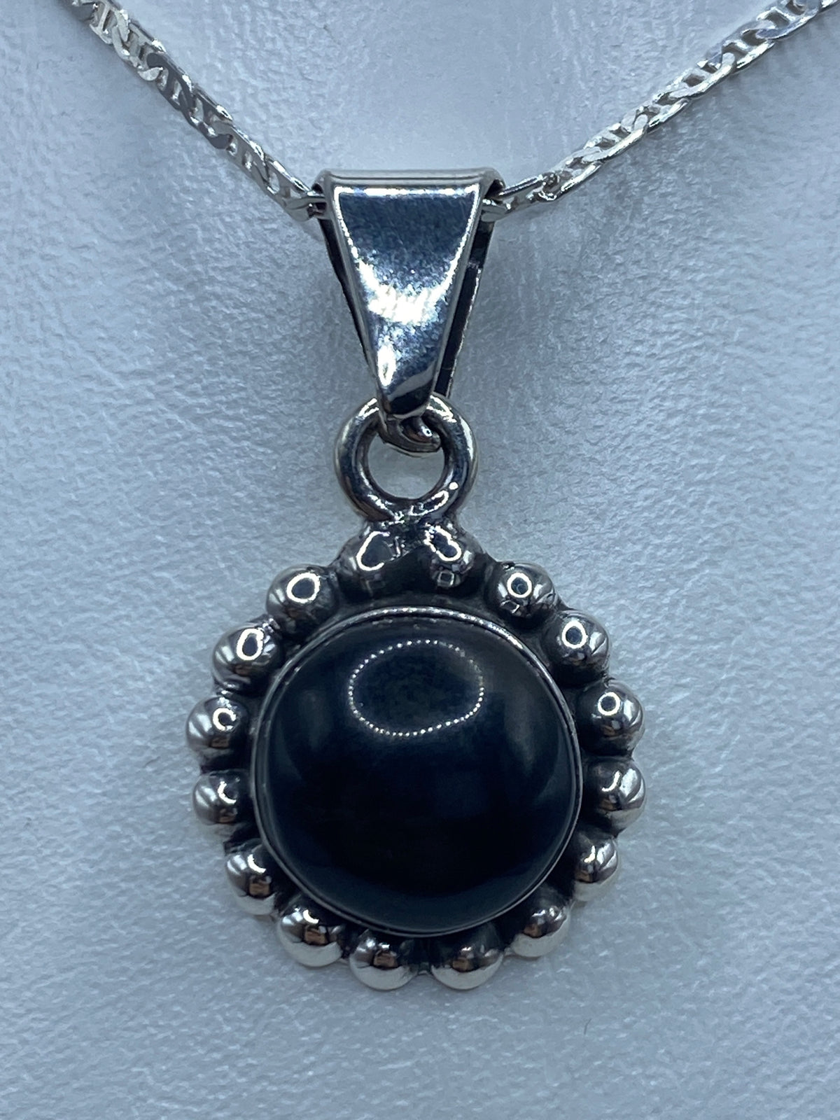 Vista frontal del dije mostrando la piedra negra pulida y el engaste de bolitas de plata