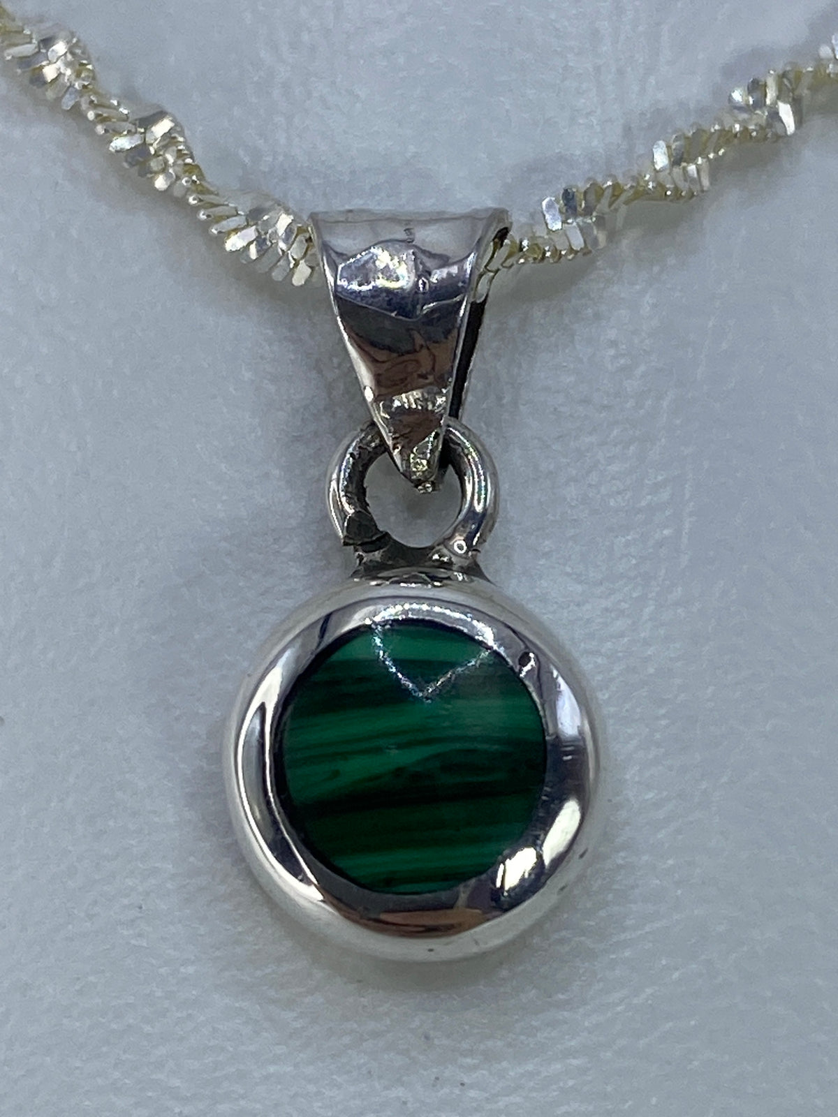 Dije de plata 925 con piedra verde engastada, colgando de cadena plateada