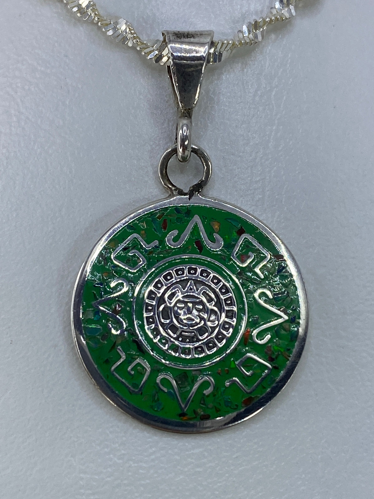 Dije de plata con calendario azteca y ópalo de fuego multicolor, colgando de cadena plateada