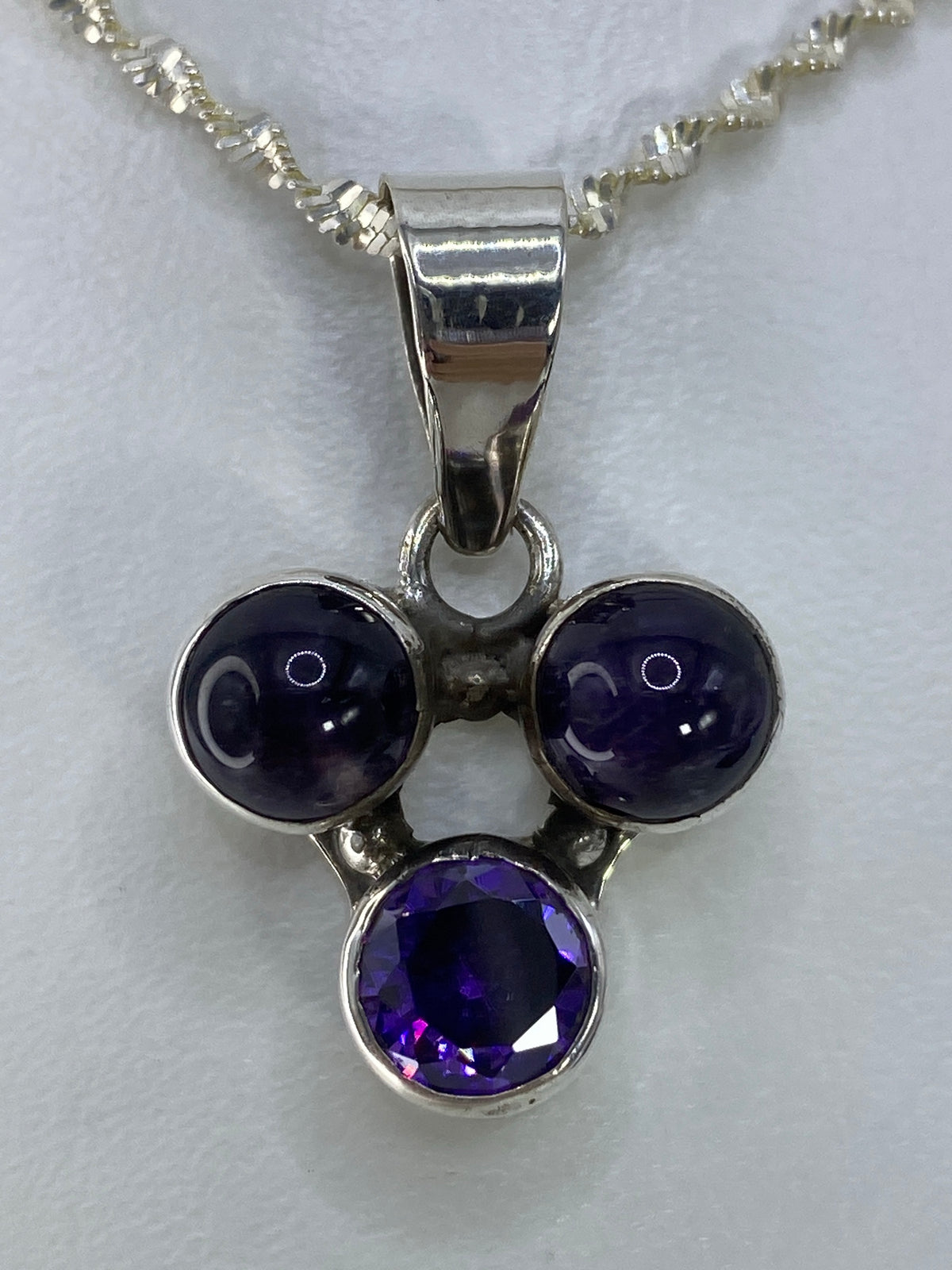 Dije de plata con tres esferas de circonia morada, dos lisas y una facetada, en cadena plateada