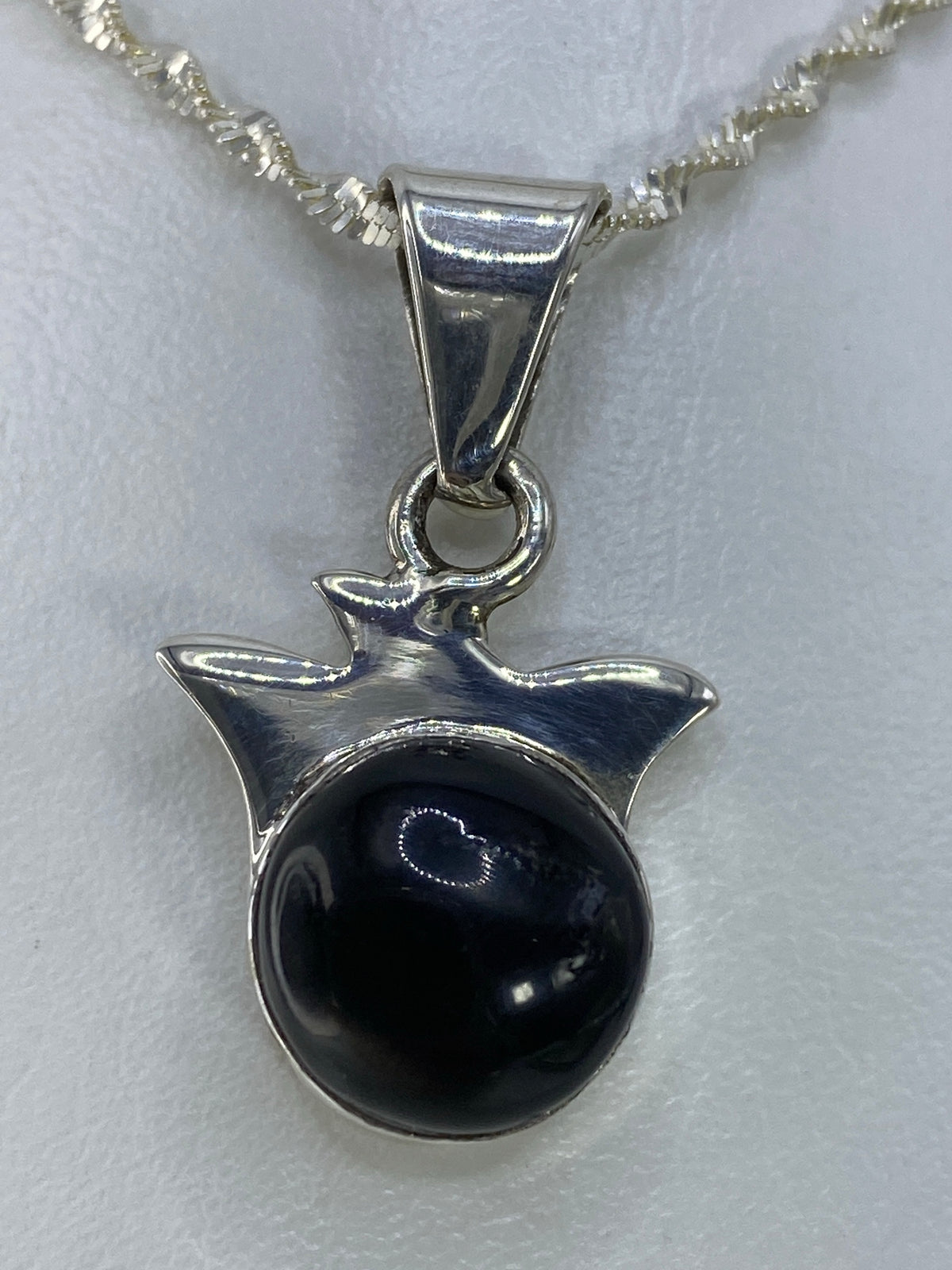 Detalle frontal del dije mostrando la piedra negra pulida y el engaste en plata 925