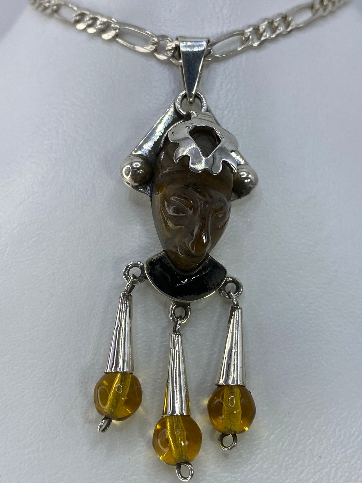 Detalle frontal del dije: ámbar café con facciones expressivas y corona de plata