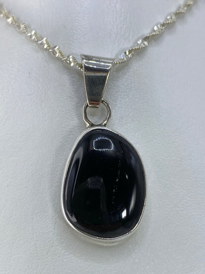 Vista frontal del dije de ónix negro de 3.6 cm mostrando el engaste en plata