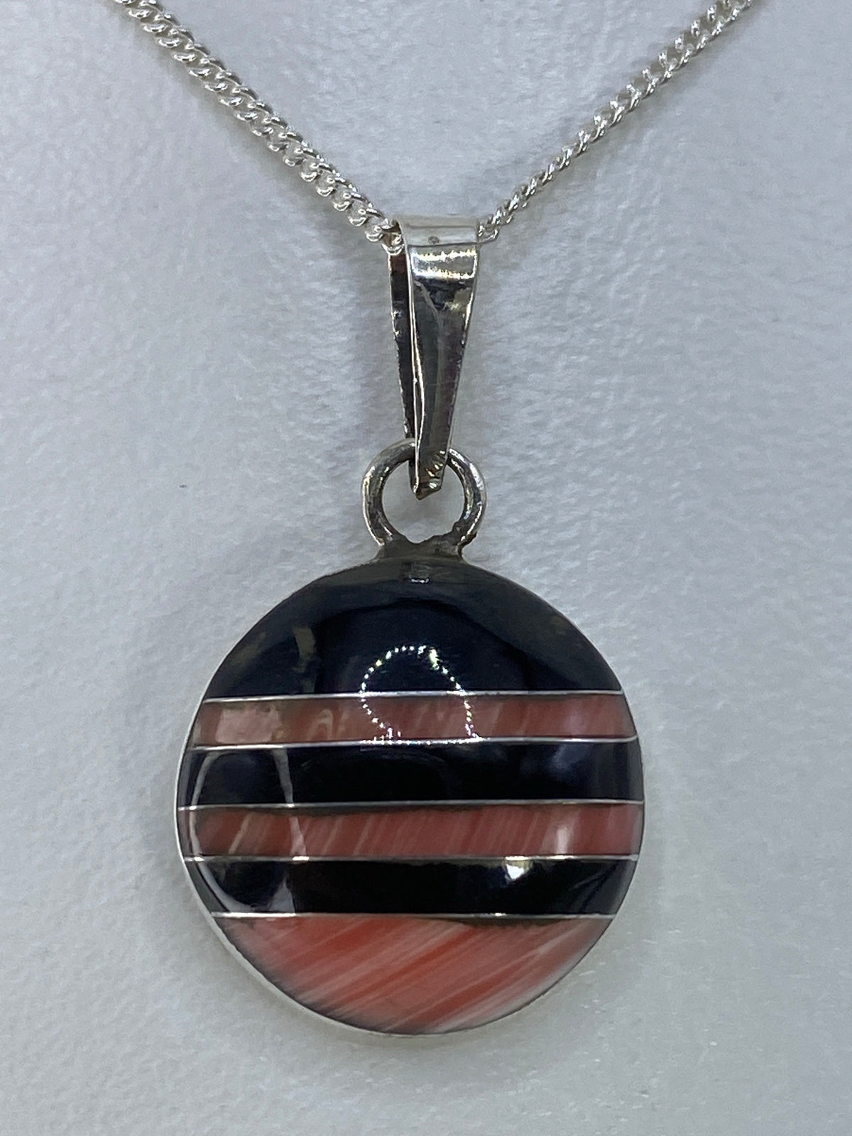 Dije de plata redondo con incrustación multicolor en franjas alternas de negro y marrón