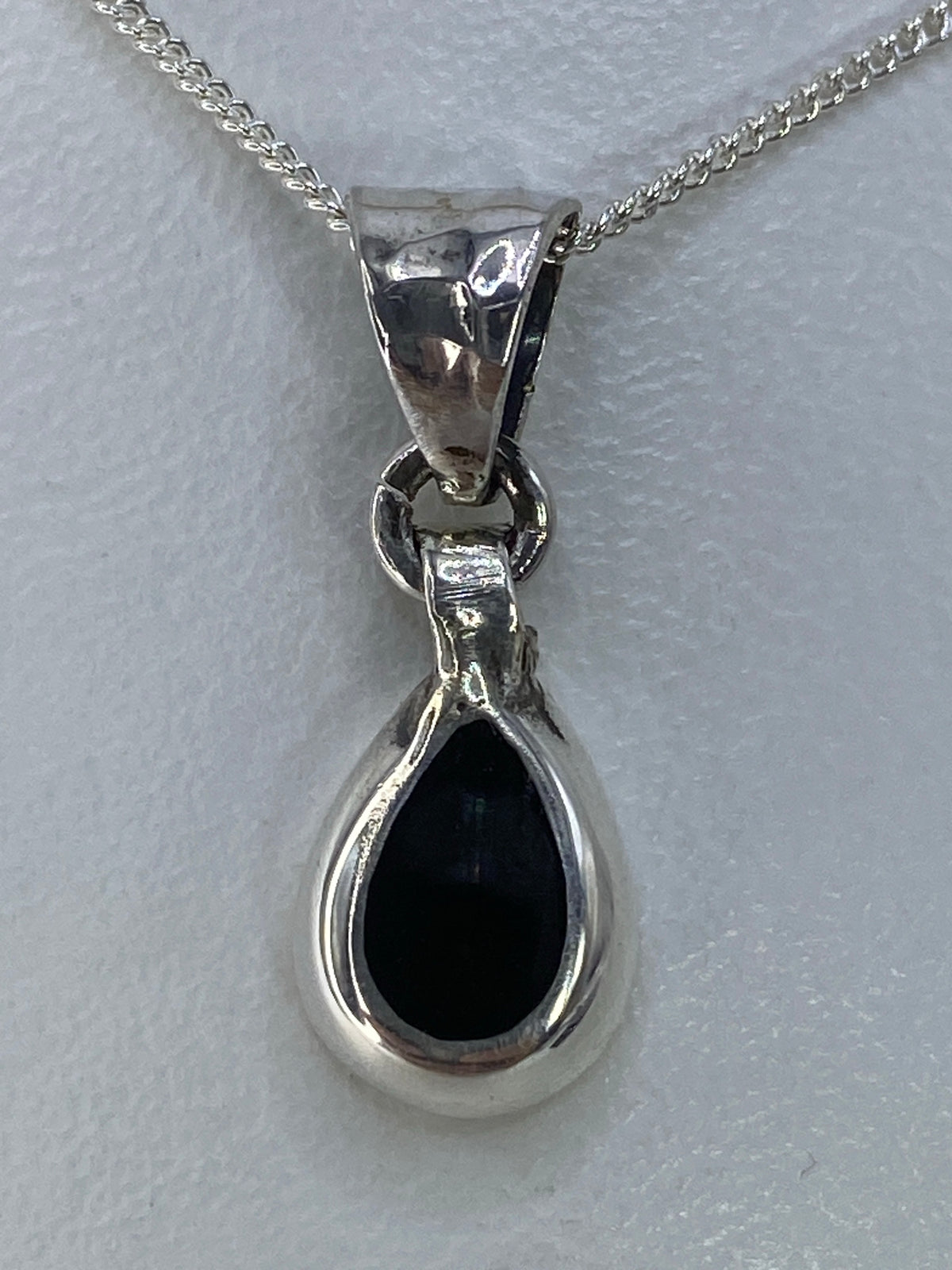 Dije de plata gota con piedra negra engastada colgando de una cadena plateada