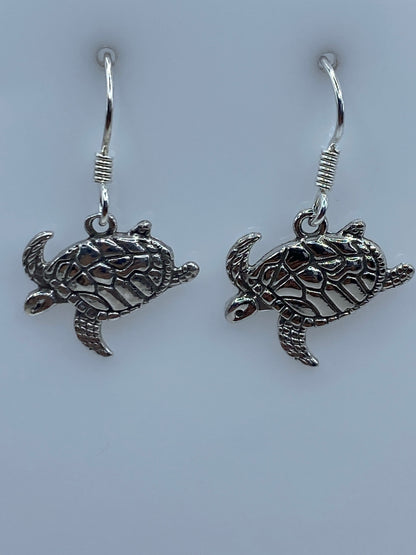Par de aretes de plata con tortuga marina en relieve repujado, colgando de ganchos plateados