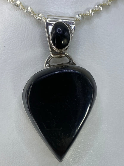 Dije de plata corazón con piedra negra pulida, colgando de una cadena de plata.