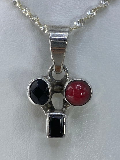 Dije de plata 925 con dos piedras engastadas: negra y roja, colgando de una cadena plateada