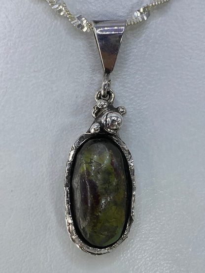 Dije de plata con piedra verde engastada, colgando de una cadena plateada