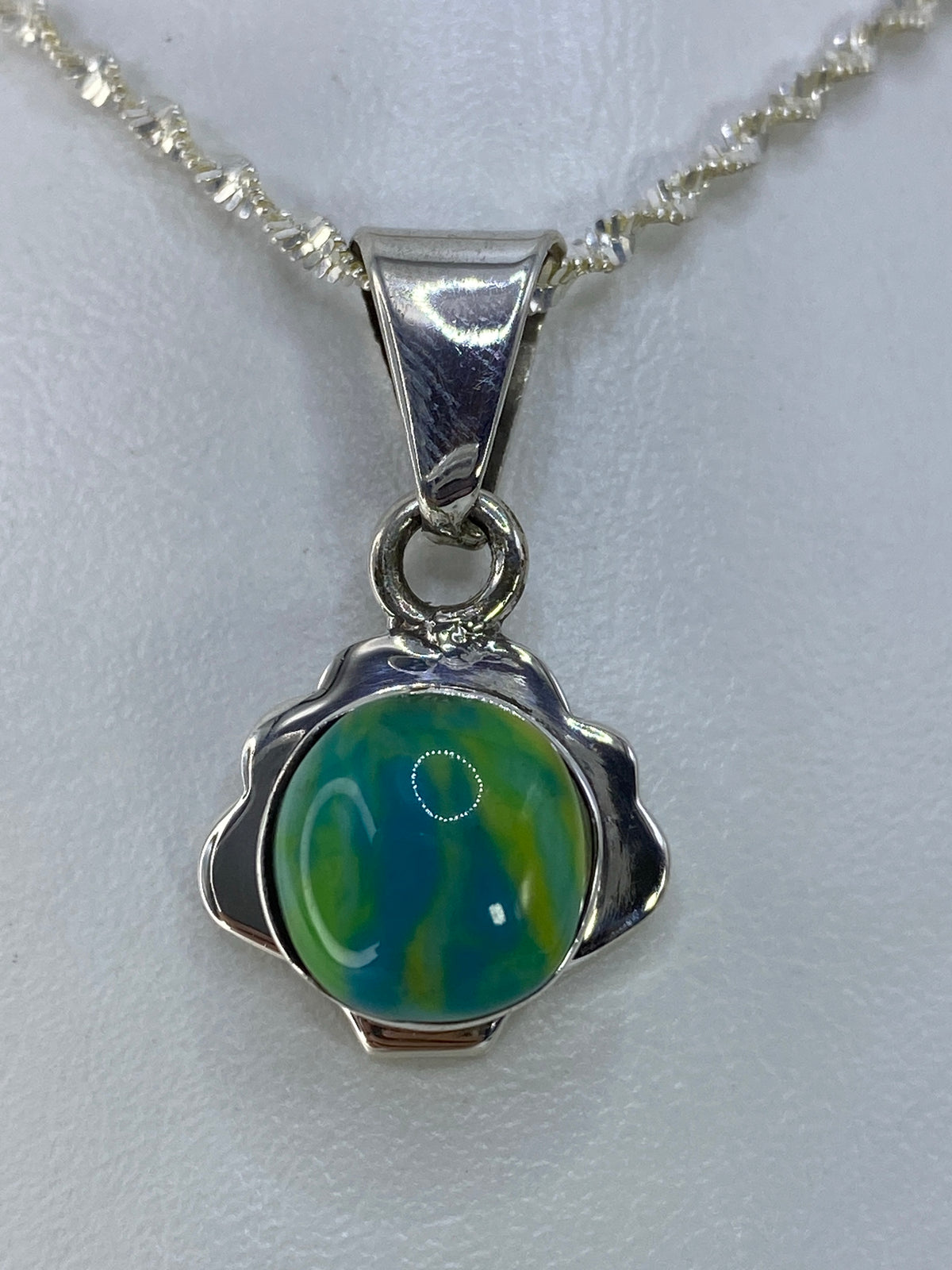 Dije de plata 925 con piedra multicolor de 3 cm de largo, colgado de cadena en la mano